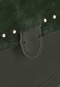 Borsa a tracolla verde in suede con base in pelle nera liscia, caratterizzata da borchie in metallo e cuciture a contrasto vicino alla chiusura a pattina.