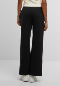 Pantalons larges noirs en tissu doux, avec une coupe décontractée et une taille élastique, associés à des baskets blanches.
