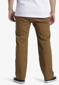 Braune Baumwollhosen mit geradem Bein; schlichtes Design; kombiniert mit schwarzen Sneakers mit weißen Akzenten und Logo.