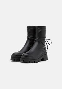 Botas negras hasta el tobillo de cuero suave con punta redondeada, suela gruesa y detalle de cordones en la parte trasera. Diseño de plataforma elevada.
