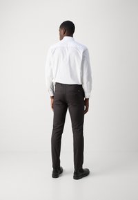 Chemise blanche à col, pantalon slim noir, mettant en avant un design épuré, une texture lisse et de légers détails sur les poches arrière. Chaussures noires.
