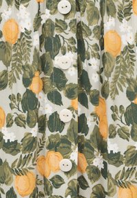 Ύφασμα με φύλλα σε πράσινους και σκουροπράσινους τόνους, μικρά λευκά λουλούδια και κίτρινα-πορτοκαλί τριαντάφυλλα, με κατακόρυφη σειρά από στρογγυλά λευκά κουμπιά.