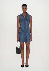 Denim kleita ar apkakles dekoltē, bez piedurknēm, divām priekšējām kabatām un pieguļošu siluetu. Valkāta ar melnu austu somu, garums virs ceļgaliem.