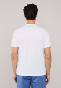 Camiseta blanca de manga corta con cuello redondo. El cuello en la parte de atrás presenta un pequeño logotipo azul. La tela parece suave y ligera.