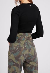 Haut noir à manches longues avec une texture côtelée et un détail réfléchissant à l'arrière, associé à un pantalon cargo haut à taille haute en camouflage vert et marron.