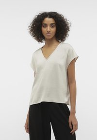 Haut beige clair en V avec des manches courtes, en tissu lisse, présentant une coupe décontractée et une texture subtile, associé à un pantalon noir.