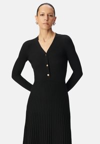 Abito nero a coste con scollo a V, maniche lunghe e tre bottoni dorati sulla parte anteriore. Silhouette elegante e aderente con una finitura testurizzata.