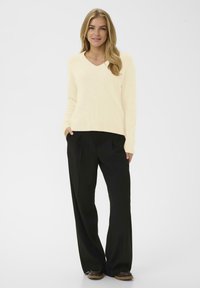 Ljust gul, v-ringad tröja med långa ärmar, bärs över lösa, svarta vida byxor. Slät textur, avslappnad passform och minimal detaljering.