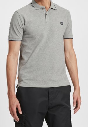 Mand iført en lysegrå kortærmet polo med sort kant på krave og ærmer, kombineret med sorte cargobukser.