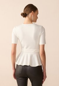 Hvit tettsittende topp med korte ermer, flared peplum-kant og bakbånd. Brukt med høy midje svarte bukser og sølv hengende øredobber.