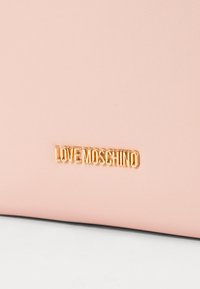 Rosa faux läderväska med en texturerad yta, med en gyllene "LOVE MOSCHINO" logotypaccent framtill.