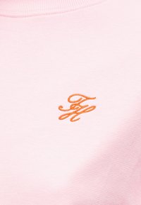 Ανοιχτό ροζ πλεκτό ύφασμα με πορτοκαλί κεντημένα αρχικά με καλλιγραφικό χαρακτήρα "FH" κοντά στο κέντρο.