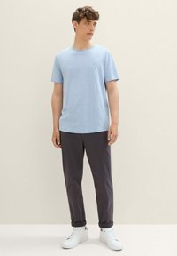Camiseta de algodón azul claro con cuello redondo, combinada con pantalones oscuros grises y zapatillas blancas. Diseño simple y casual, sin patrones.