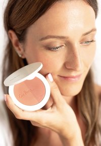 Ronde blushcompact met twee tinten roze. De buitenkant is wit met een gladde afwerking; merknaam in reliëf op de voorkant.