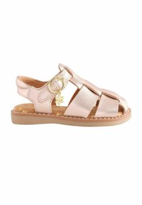 Pink metallic sandal med krydsede remme, åben tå, gylden blomst som dekorativ detalje og en tanfarvet sål med syningsdetaljer.