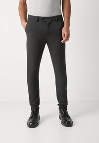 Donkergrijze, op maat gemaakte broek met een gladde textuur, een strakke pasvorm, voorzakken en een knoopsluiting, gecombineerd met zwarte veterschoenen.