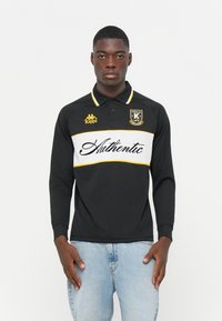 Polo a maniche lunghe nero con striscia orizzontale bianca e gialla, con logo "Authentic" e marchio Kappa sul petto.