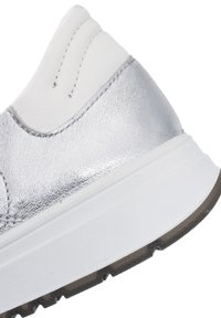 Close-up of silver and white sneaker heel with textured sole and detailed stitching on upper part.