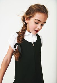 Rochie neagră cu fermoar frontal, cu un capac de fermoar în formă de inimă și guler alb. Părul este coafat într-o coadă împletită, cu un accent de panglică neagră.