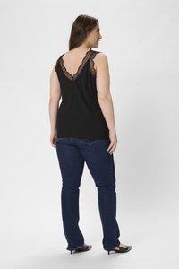 Top sans manches noir avec une délicate bordure en dentelle le long du dos en V, associé à un jean en denim bleu foncé et des chaussures noires à talons pointus.
