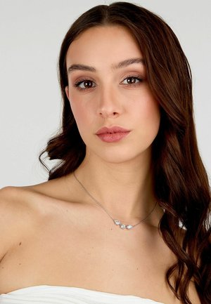 Collana d'argento con tre gemme chiare e scintillanti incastonate in una catena delicata. Il modello indossa un top senza spalline, mostrando collo e clavicola.