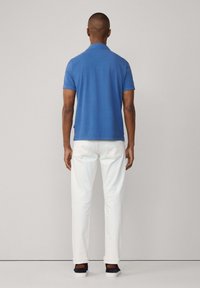 Polo de algodón azul con mangas cortas, combinado con pantalones blancos y zapatillas negras. Aberturas laterales visibles en el dobladillo de la camiseta.