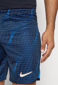 Pantalones cortos azul y negro con un diseño de cuadros, con cintura elástica y un logo dorado de Nike en el dobladillo izquierdo.