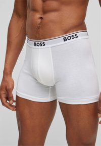 Weiße Boxershorts aus weichem Stoff, mit einem schwarzen "BOSS"-Logo am Bund, in enger Passform und mit flachen Nähten.