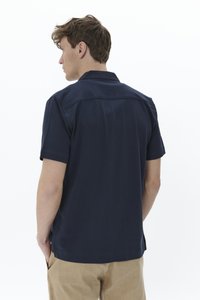 Polo shirt marine à manches courtes en tissu doux, avec un col boutonné et un ourlet droit, porté avec un pantalon beige clair.