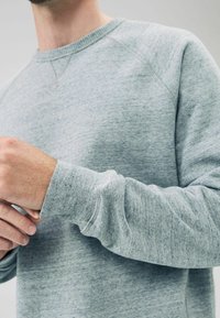 Lys grå sweatshirt med ribbede manchetter, rund halsudskæring og struktureret stof. Har raglanærmer og et blødt, afslappet design.