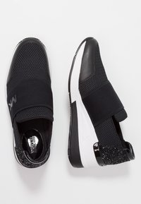 Chaussures de sport noires avec tige en mesh, bande élastique et accent texturé au talon. Semelle intermédiaire blanche, design épuré et semelle extérieure en caoutchouc solide.