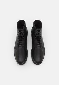 Bottines en cuir noir avec une finition texturée, bout rond, laçage traditionnel et détail de fermeture éclair sur le côté. Doublure intérieure lisse.