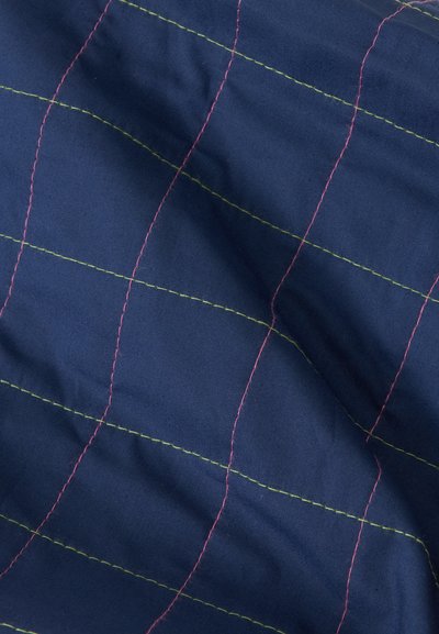 Gros plan d'un tissu bleu foncé avec un motif en grille cousu avec un fil rose et vert clair alternés.