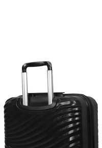 Black hardshell suitcase with wave pattern, telescopic aluminum handle, and a smooth finish. Zipper closure at the top.