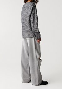 Haut gris à manches longues avec un motif texturé en losanges ; associé à un jean gris clair ample avec des accents usés et des poches.