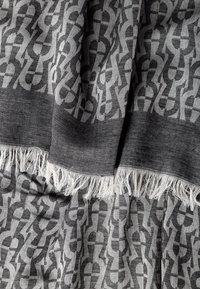 Textil gris con un diseño geométrico y bordes con flecos. La tela tiene una textura suave y un intrincado detalle.