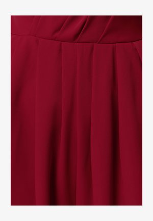 Vīna sarkanā auduma ar vertikālām locījuma krokām, kas veido plūstošu, teksturētu rakstu un maigus ēnas auduma virsmā.