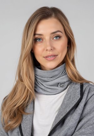 Jeune femme aux longs cheveux blonds portant un tour de cou gris, une chemise blanche et une veste grise texturée sur un fond uni.