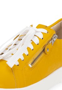 Yellow leather sneaker with white laces, textured upper, side zipper detail, and a rubber sole. Close-up view of the shoe's features.