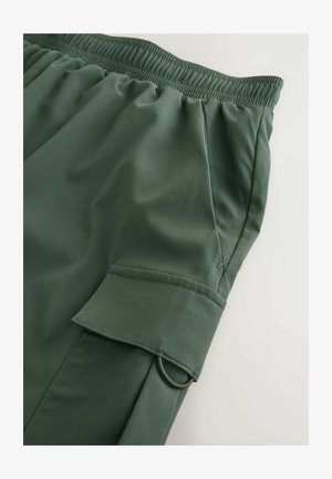 Olivgrüne Sportshorts mit einem elastischen Bund, Seitentasche und einem sichtbaren Ringakzent an der Taschenklappe. Glattes, leichtes Material.