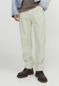 Beige bomuldsbukser med en løs pasform, båret med mørkebrune snørebåndsstøvler. Den øverste del er delvist synlig, med en brun skjorte og en denimjakke.