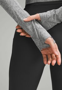 Graues Langarmoberteil mit Daumenlöchern, strukturierter Stoff. Schwarze gerippte Leggings. Sichtbare Hand hält den Ärmel, die Finger zeigen einen natürlichen Griff.