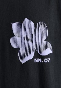 Fleur stylisée blanche avec des rayures noires verticales et le texte "NN. 07" sur un fond en tissu noir.