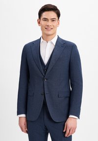Dunkelblauer Anzug aus strukturiertem Stoff, einreihiges Design, mit Reverskragen und zwei Vordertaschen. Kombiniert mit einem weißen Hemd.