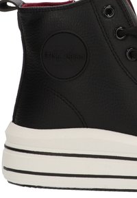 Zapatilla alta negra con superficie texturizada, suela blanca con rayas negras, ojales para cordones y un parche de logo circular en el lateral.