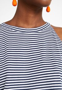 Top canotta a righe realizzato in tessuto leggero, con righe orizzontali blu navy e bianche, collo rotondo e spalle scoperte.
