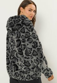 Veste en fausse fourrure grise avec imprimé léopard noir, dotée d'une capuche, de manches longues et d'un ourlet élastique. Texture douce et design décontracté.