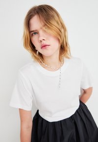 Witte katoenen t-shirt met korte mouwen, met een ontspannen pasvorm. Gecombineerd met een zwarte textuurrok en een zilveren kettinghalsketting als accent.