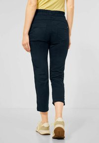 Mörkblå, korta byxor med elastisk midja, som har två bakfickor och en slät yta. I kombination med ljusa träningsskor.