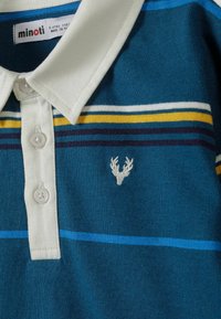 Turkusowa polo w paski z białym kołnierzykiem. Posiada niebieskie, żółte i ciemne paski. Haftowane logo rogów jelenia na piersi.